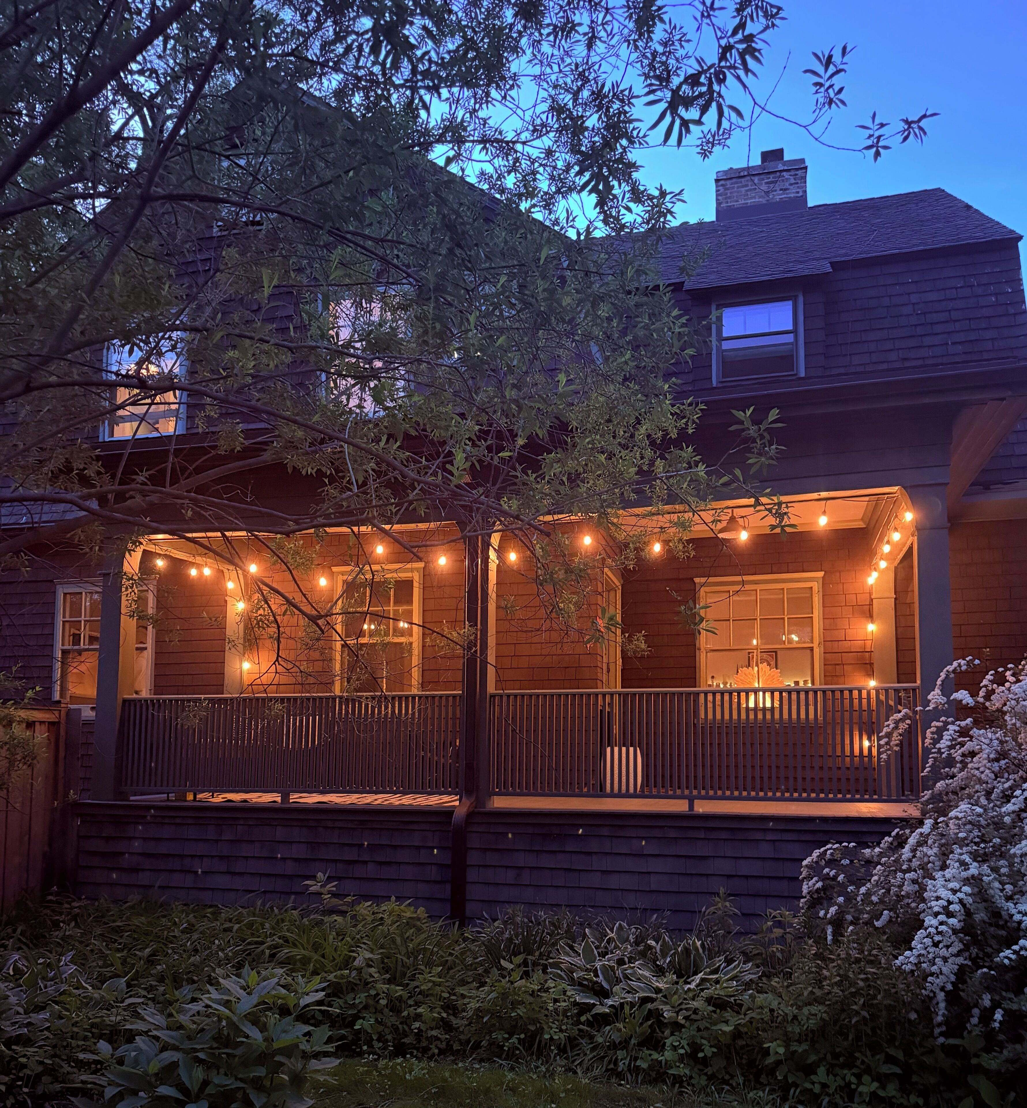 A house with a porch, string lights, and a brick chimney.