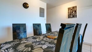 A dining area with a table, chairs, a wall clock, and a cityscape painting. - La Kaz Rouge - Climatisation - Plage (Saint-Paul)