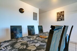 A dining area with a table, chairs, a wall clock, and a cityscape painting. - La Kaz Rouge - Climatisation - Plage (Saint-Paul)