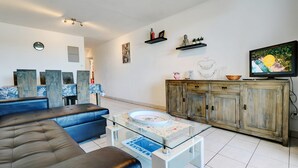 A living room with a sofa, coffee table, TV, and decorative items. - La Kaz Rouge - Climatisation - Plage (Saint-Paul)