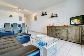 A living room with a sofa, coffee table, TV, and decorative items. - La Kaz Rouge - Climatisation - Plage (Saint-Paul)