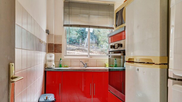 A compact kitchen with red cabinets, a stainless steel sink, and a built-in oven. - La Kaz Rouge - Climatisation - Plage (Saint-Paul)