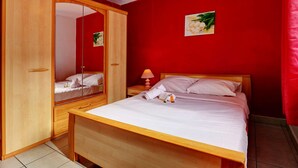 A bedroom with a wooden bed, a nightstand, a mirror, and a red wall. - La Kaz Rouge - Climatisation - Plage (Saint-Paul)