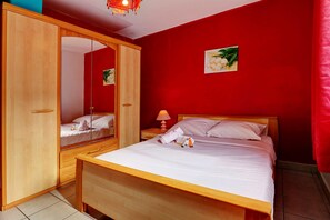 A bedroom with a wooden bed, a nightstand, a mirror, and a red wall. - La Kaz Rouge - Climatisation - Plage (Saint-Paul)