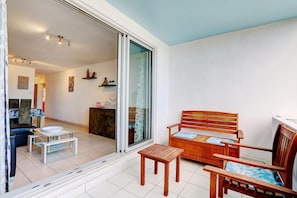A room with a wooden bench, a small table, and a sliding glass door leading to a dining area with a table and chairs. - La Kaz Rouge - Climatisation - Plage (Saint-Paul)