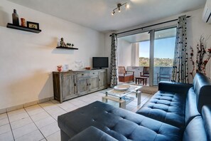 A modern living room with a sofa, a coffee table, a TV, and a sliding glass door leading to an outdoor area. - La Kaz Rouge - Climatisation - Plage (Saint-Paul)