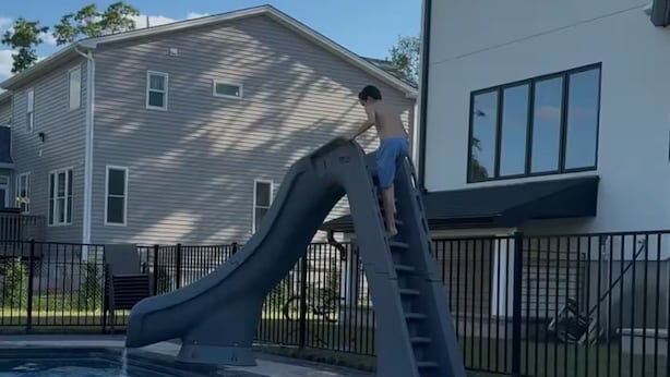 A swimming pool with a slide, a house in the background, and a clear sky.