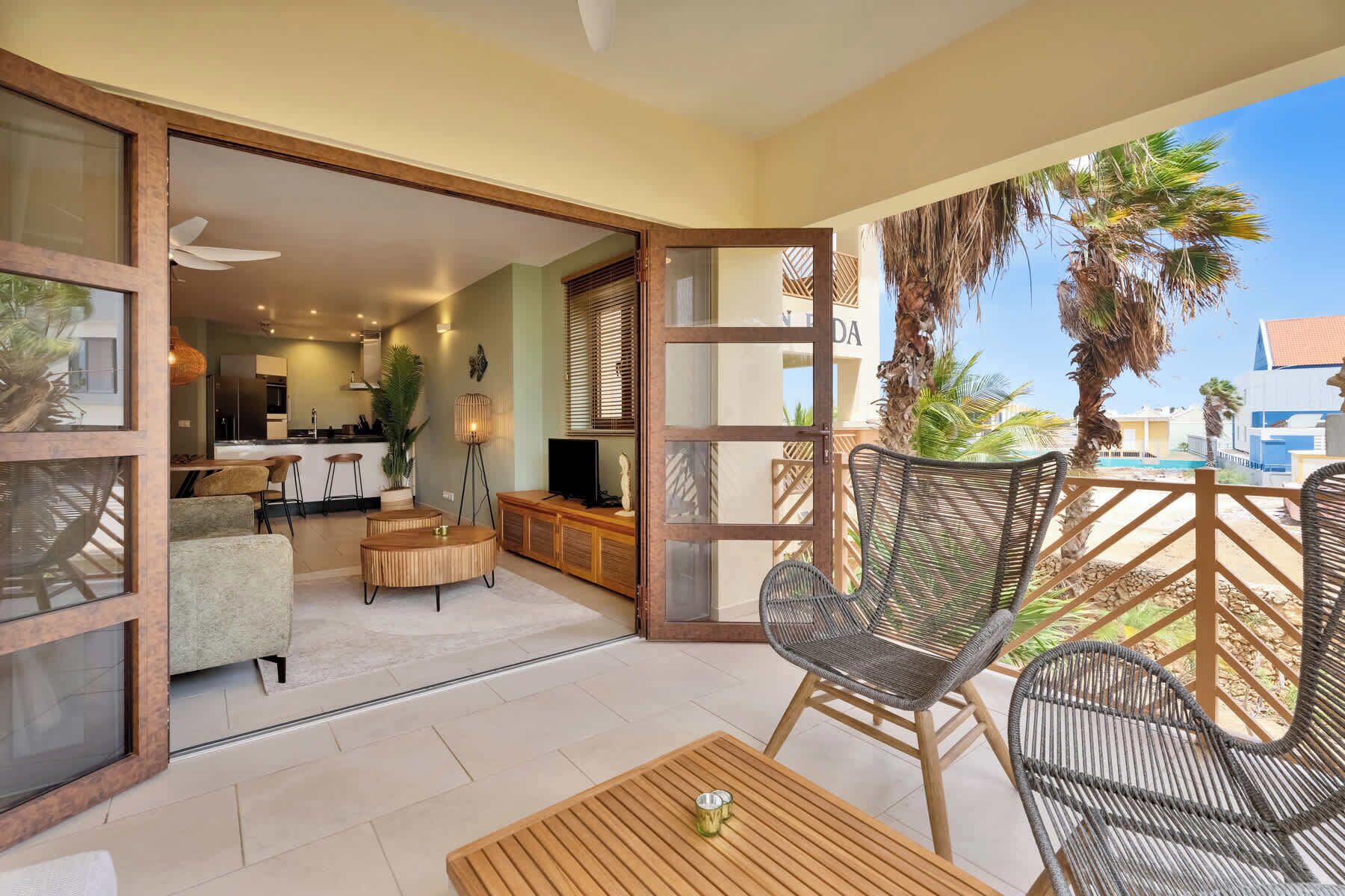 A balcony with wicker furniture, a dining area with a bar, and a view of palm trees and buildings.