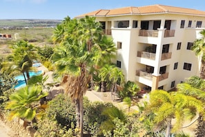 Ett hotell med flera våningar, balkonger, en swimmingpool och frodig grönska.