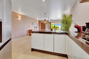 Une cuisine moderne dotée d’un îlot central, d’un ventilateur de plafond et offrant une vue sur l’extérieur.