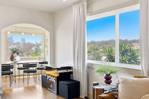 A modern living room with a dining area, large windows with city views, and a visible Atari Pong gaming console. - Golden Hill Escape Near Balboa Park & Zoo (San Diego)
