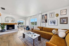 A modern living room with a fireplace, a sofa, a coffee table, and a dining area with natural light. - Golden Hill Escape Near Balboa Park & Zoo (San Diego)