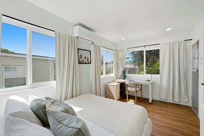A modern bedroom with a large bed, a desk, and a view of greenery. - Hot Tub & Arcade Escape Near Balboa Park (San Diego)