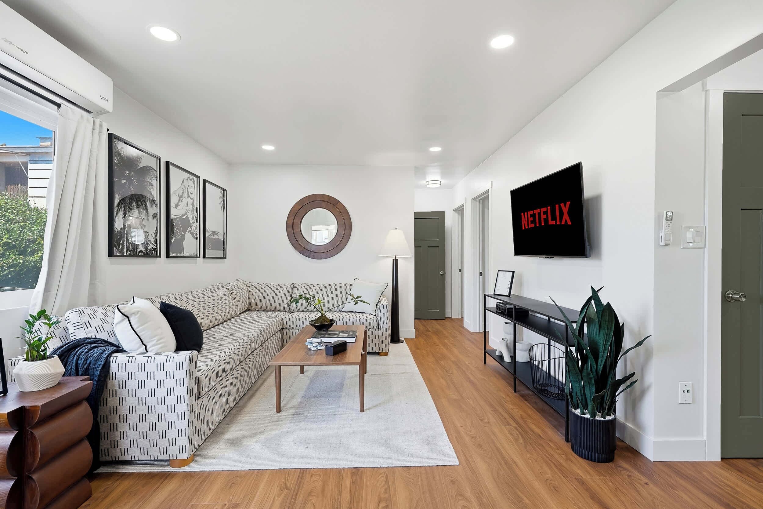 A modern living room with a sectional sofa, a coffee table, a TV mounted on the wall, and a large mirror.