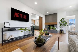 A modern living room with a Netflix sign, a fireplace, and a view of the city. - Hot Tub & Arcade Escape Near Balboa Park (San Diego)