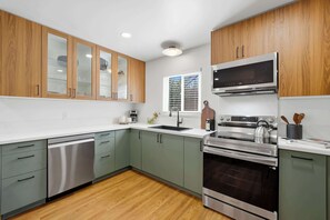 A modern kitchen with stainless steel appliances, wooden cabinets, and a window with blinds. - Downtown San Diego Stay with Hot Tub & BBQ (San Diego)