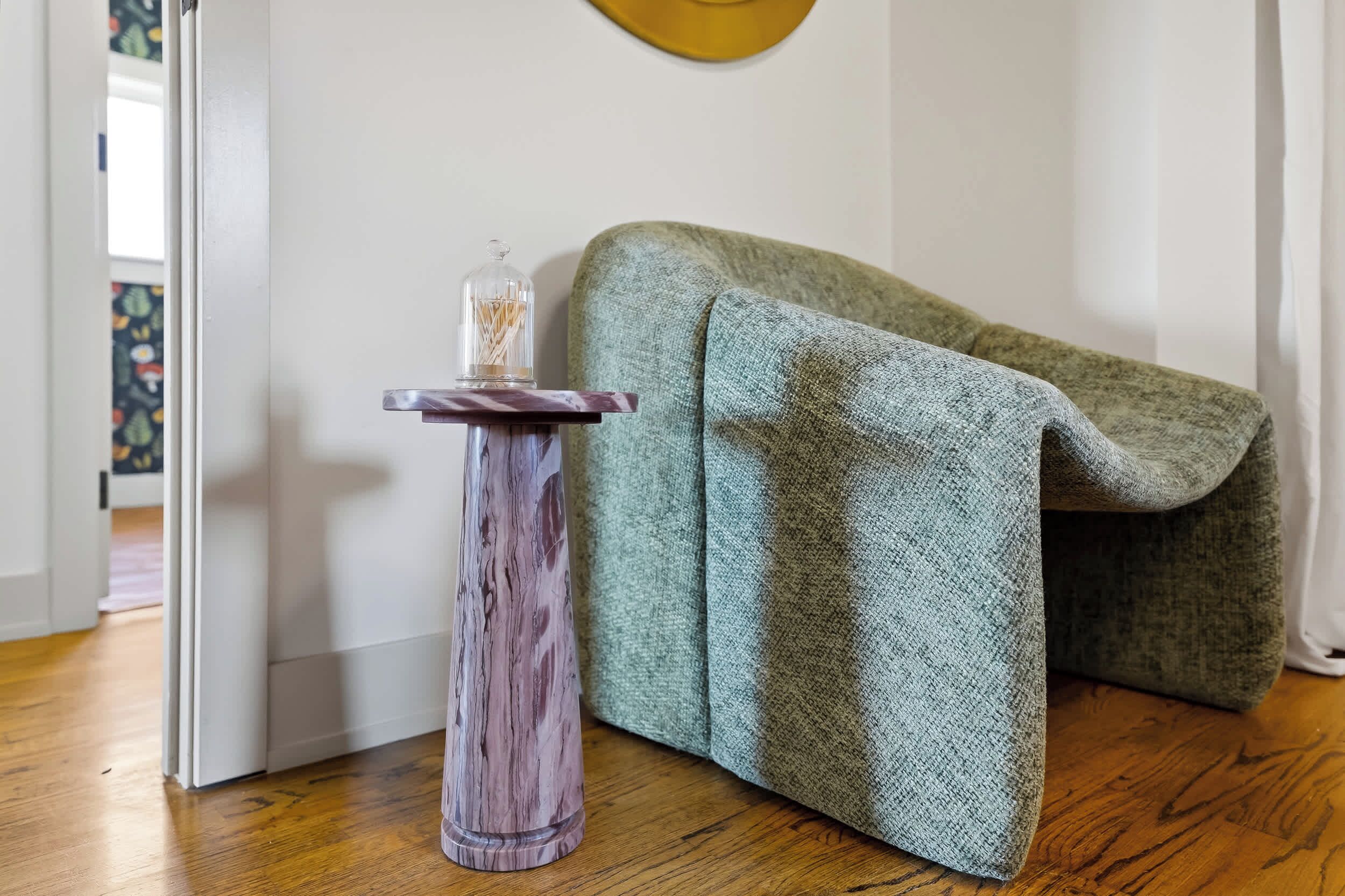 Ein Zimmer mit einem grünen Sofa, einem kleinen Holztisch und einem Glasbehälter sowie einer weißen Tür.