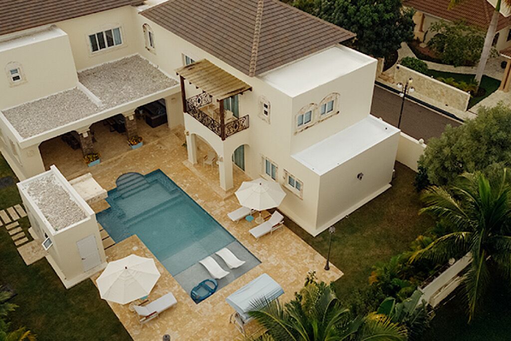Una casa de dos pisos con piscina, mobiliario exterior y un patio cubierto.