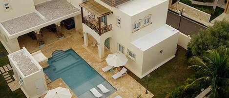 Una casa de dos pisos con piscina, mobiliario exterior y un patio cubierto.