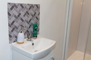 Een badkamer met een witte wastafel, een groene fles en een achterwand betegeld met een herringbonte tegelvloer.