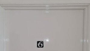 Uma porta branca com uma etiqueta com o número 6 e um interfone.