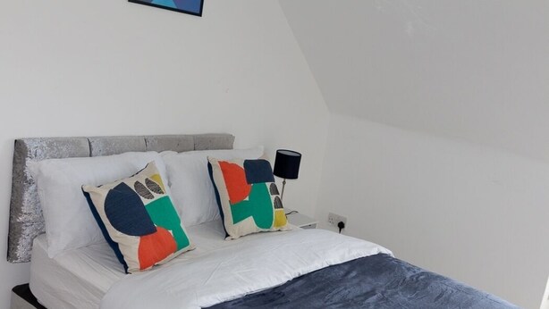 Um quarto com uma cama, almofadas, uma luminária e um quadro na parede.