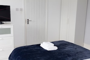 Ein Schlafzimmer mit einem Bett, einem Fernseher auf einer Kommode und einem weißen Kleiderschrank.
