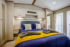 A bedroom with a bed, a headboard, a nightstand, a wardrobe, and a window with curtains. - Kernow Lodge Luxe Seaside Cabin Wraparound Deck (Milford on Sea)