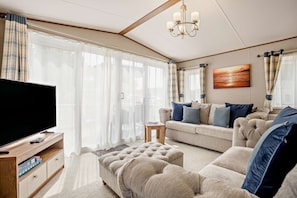 Ein Wohnzimmer mit Fernseher, Sofa, Hocker und einem Gemälde an der Wand.