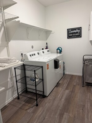 A laundry room with a stacked washer and dryer, a metal drying rack, and a sign on the wall. - Spacious 5-bedroom Family House in Spring near George Bush Airport (Spring)