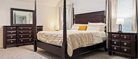 A four-poster bed with a dark finish, flanked by two nightstands with drawers, a mirror, and a floor lamp.