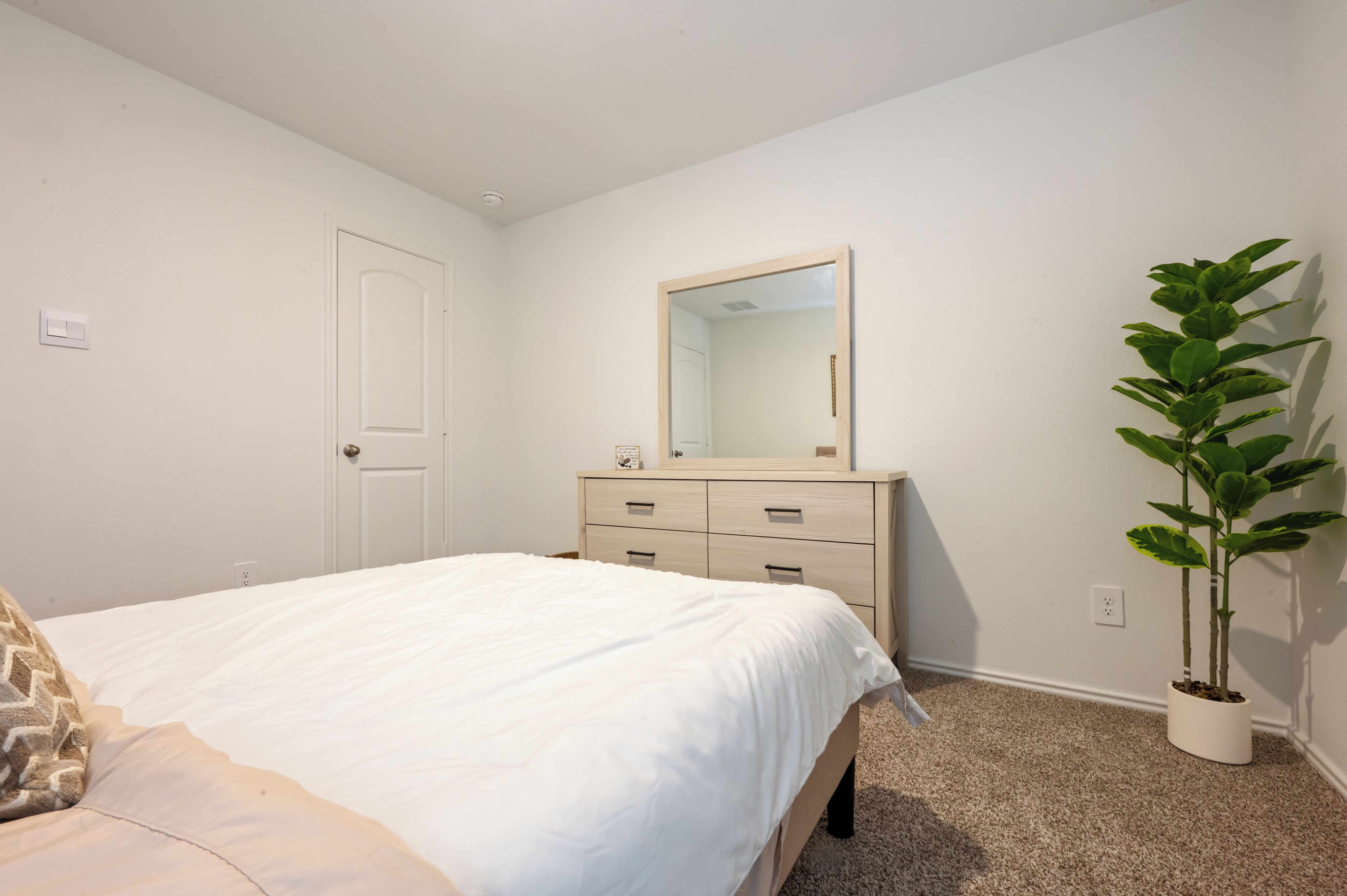 Een slaapkamer met een bed, een dressoir, een spiegel en een potplant.