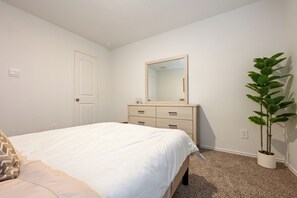 Een slaapkamer met een bed, een dressoir, een spiegel en een potplant.