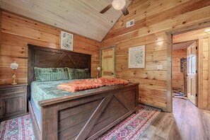 Ein Holzinterieur mit einem Bett, einem Nachttisch, einer Lampe und einer Tür zu einem anderen Raum.
