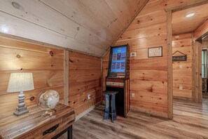 Ein Holzinterieur mit einem Globus auf einem Tisch, einem kleinen Schreibtisch und einem an der Wand befestigten Bildschirm, der ein Spiel zeigt.
