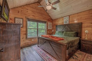 Ein Schlafzimmer einer Holzhütte mit Bett, Deckenventilator, Fenster und Wandleuchte.