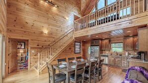 A wooden cabin interior with a dining area, kitchen, and a staircase leading to a loft. - Near Downtown Gburg, Theater, Views, Trailer Parking,Dogs OK! (Gatlinburg)