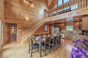 A wooden cabin interior with a dining area, kitchen, and a staircase leading to a loft. - Near Downtown Gburg, Theater, Views, Trailer Parking,Dogs OK! (Gatlinburg)