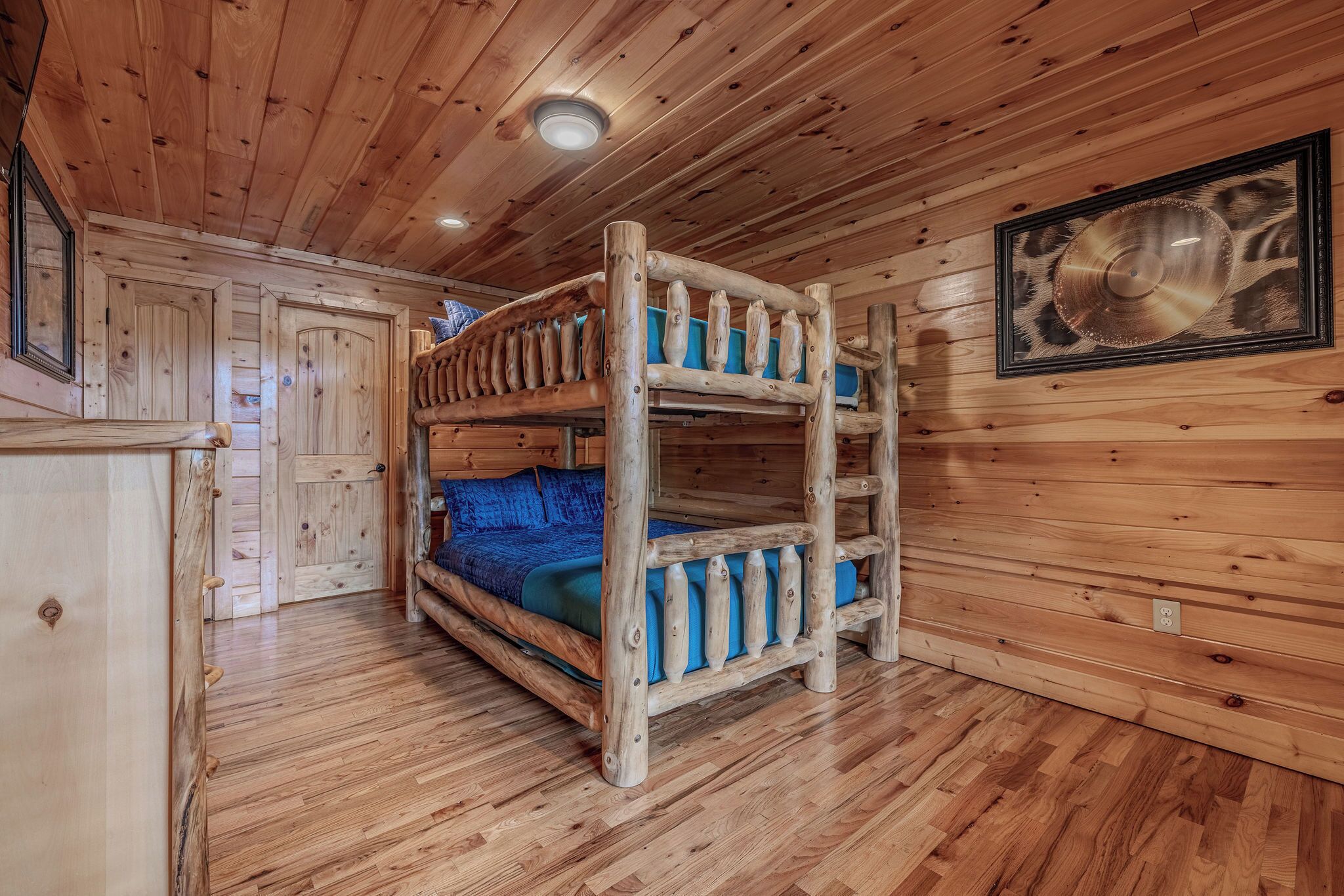 Un lit superposé en bois avec un matelas bleu, dans une chambre de style cabane, aux murs et au plancher en bois.