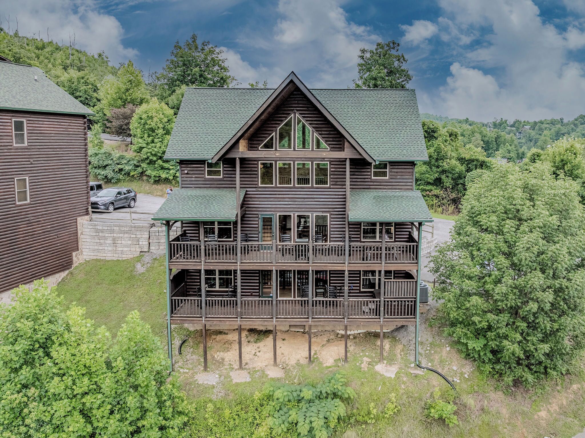 Eine zweistöckige Blockhütte mit einem grünen Dach, mehreren Balkonen und einer umliegenden bewaldeten Gegend.