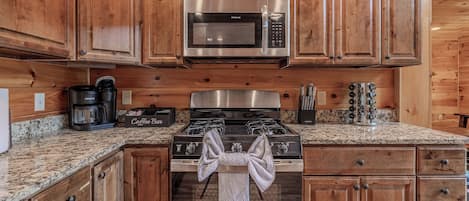 Una cocina con armarios de madera, un microondas de acero inoxidable, una cafetera y una estufa con una toalla.