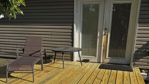 Puisesta laudasta rakennettu terassi, jossa on tuoli ja pöytä, liukuovet ja julkisivulaudoilla verhoiltu talo.