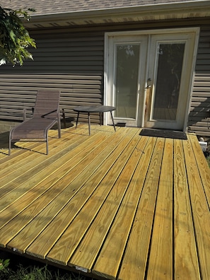 Eine Holzterrasse mit Stuhl und Tisch, eine Schiebetür aus Glas und ein Haus mit Holzverkleidung.