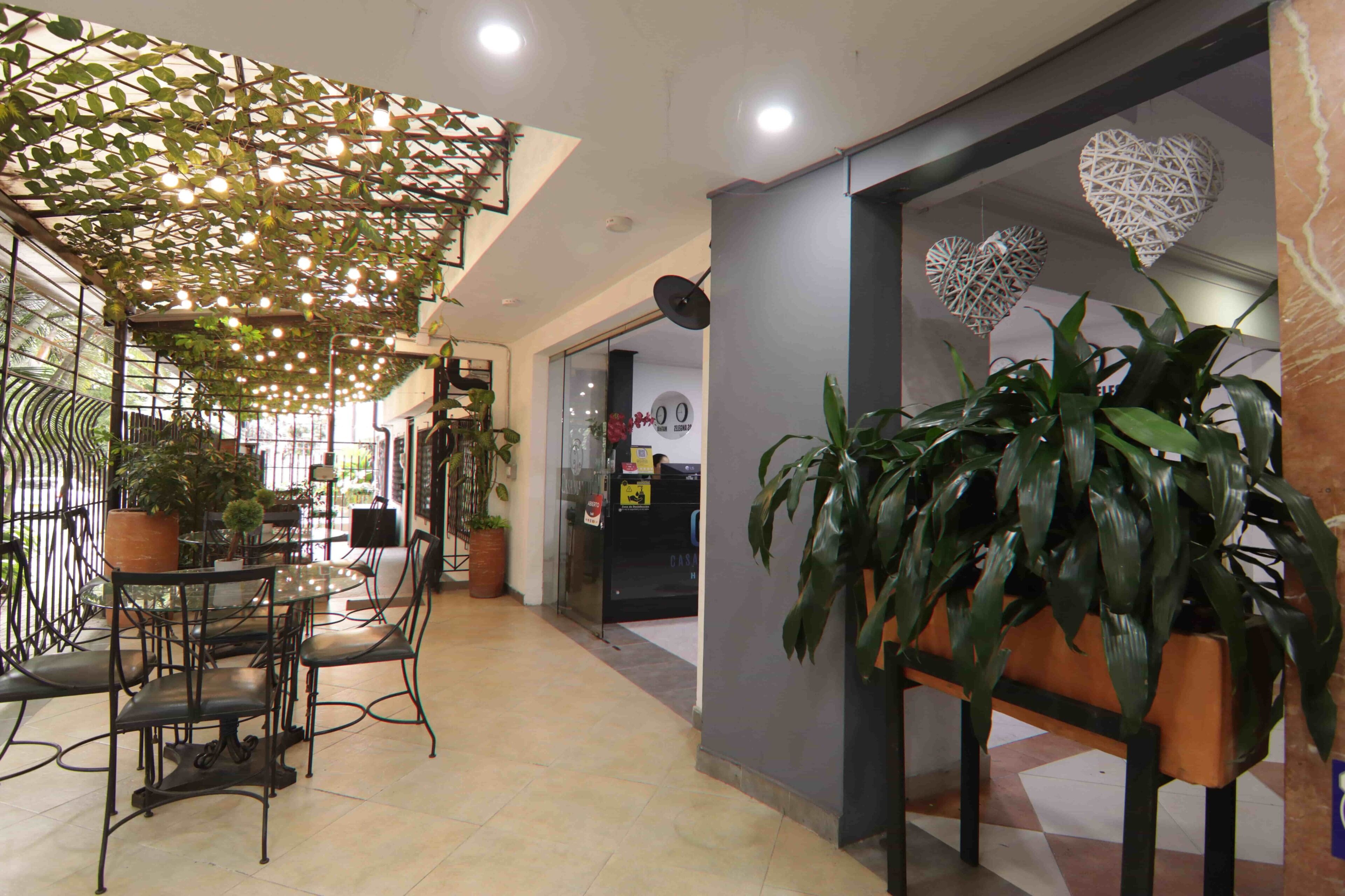A cafe with tables and chairs, a reception desk, and decorative plants.