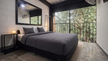 Un dormitorio moderno con una cama grande, una mesita de noche, un espejo montado en la pared y un balcón con vistas a zonas verdes.