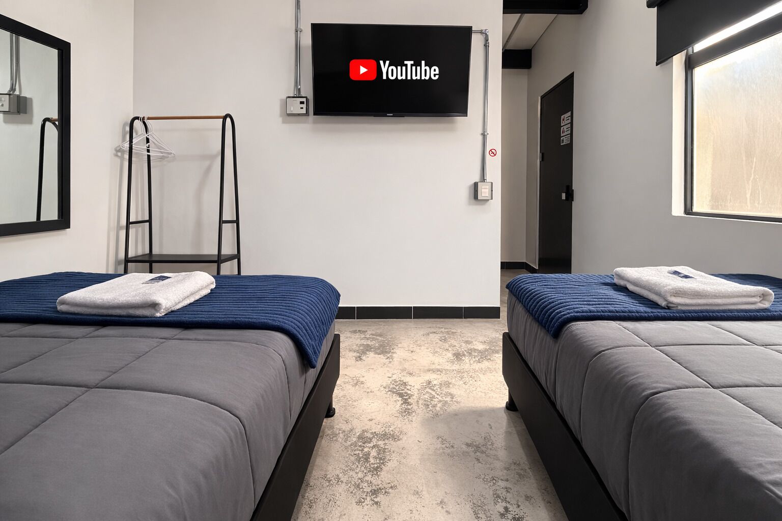 A hotel room with two beds, a TV mounted on the wall, and a view of the hallway.