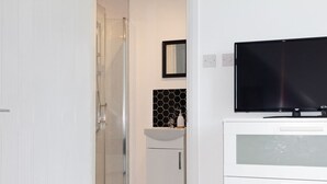 Une salle de bain équipée d’une douche, d’un lavabo et d’un téléviseur fixé sur un meuble.