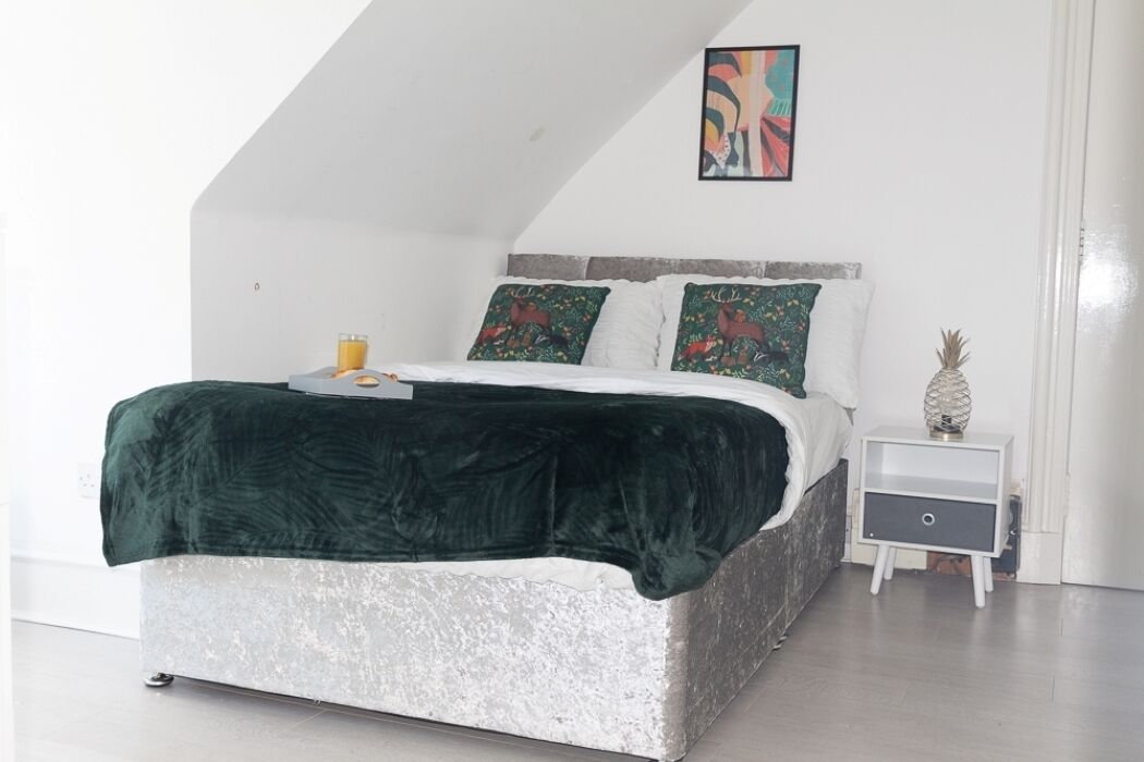 Ein Schlafzimmer mit Bett, Kissen, einem Nachttisch und einem Wandbild.
