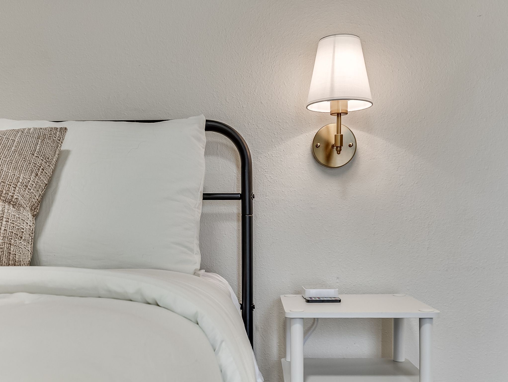 Un lit avec une tête de lit, une table de chevet avec une lampe et un luminaire fixé au mur.