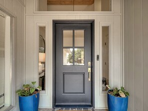 A dark grey door with a glass panel, flanked by two blue planters with plants, and a small step leading to the entrance.
